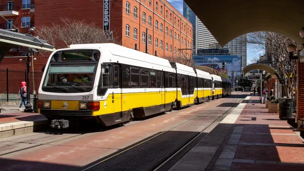 White and yellow DART light rail train in Dallas, Texas with brick building in background.